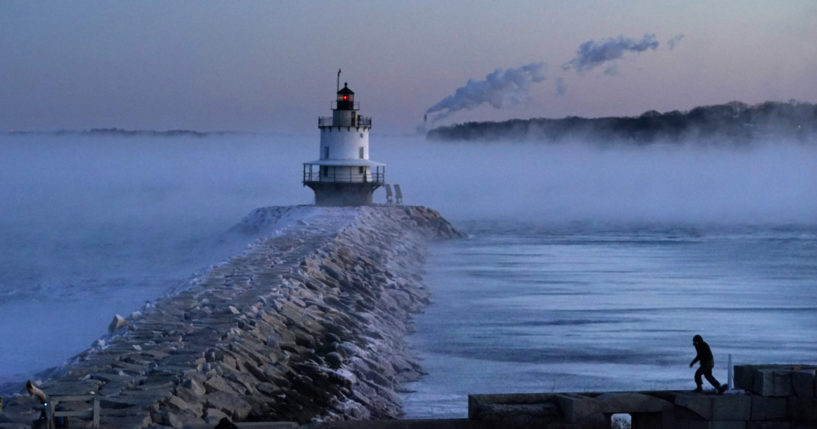 A man walks on a sea wall near Spring Point Ledge Light in South Portland, Maine, on Saturday. Morning temperatures there hovered near 10 below zero.