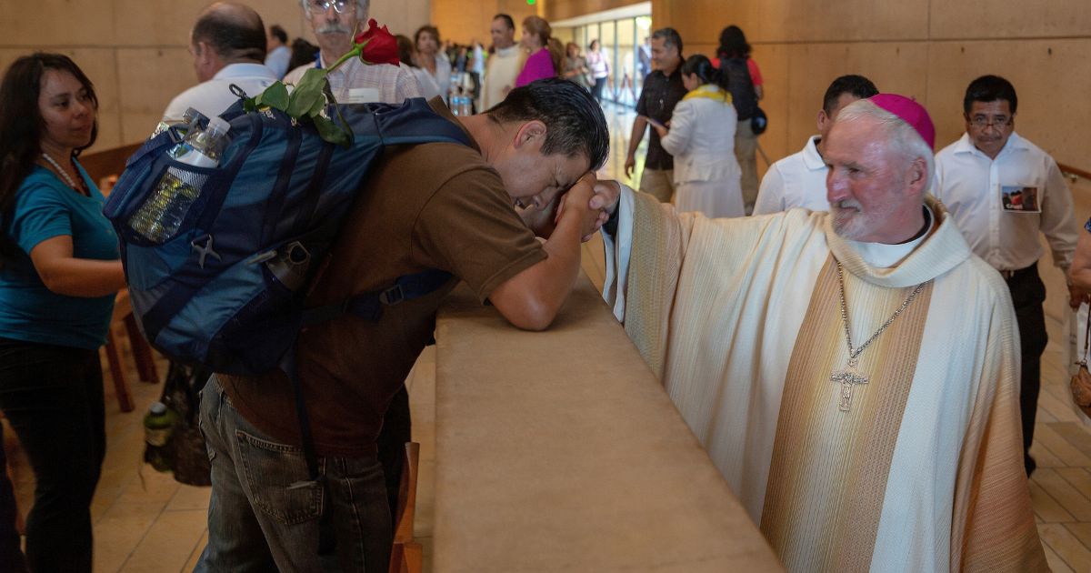 Auxiliary Bishop David O'Connell, right, from the San Gabriel Pastoral Region, is revered by an unidentified pilgrim, left, after a special "Mass in Recognition of All Immigrants'' at the Los Angeles Cathedral of Our Lady of Angels in Los Angeles on June 24, 2018.