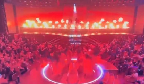 A scene from the Grammys shows dancers suffused in red lighting with fire flaring on stage.