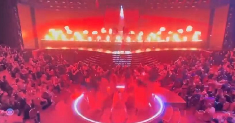 A scene from the Grammys shows dancers suffused in red lighting with fire flaring on stage.