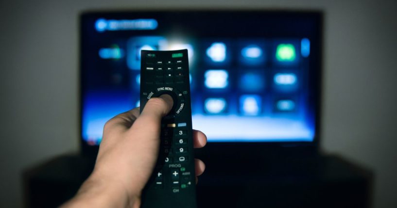A man points a remote at a television in this stock image.