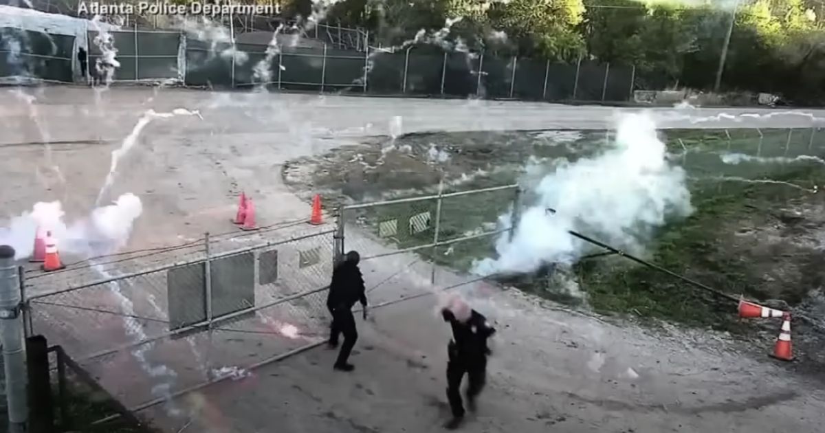 Police officers struggle to secure a gate as they are bombarded with fireworks.