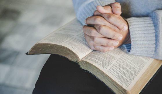 A stock photo shows a woman with her hands folded in prayer on a Bible.