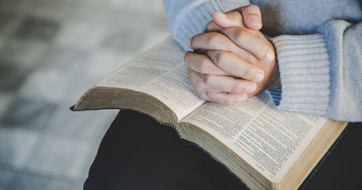A stock photo shows a woman with her hands folded in prayer on a Bible.