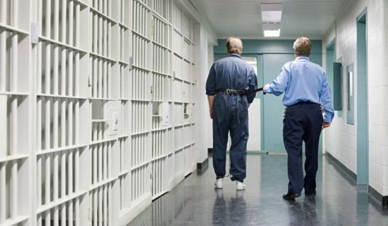 A stock photo shows a prison inmate being led by a guard.