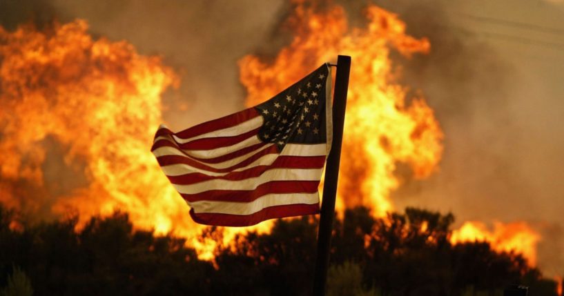An American flag is seen in the foreground as a wildfire burns near Acton, California, on July 20, 2004.