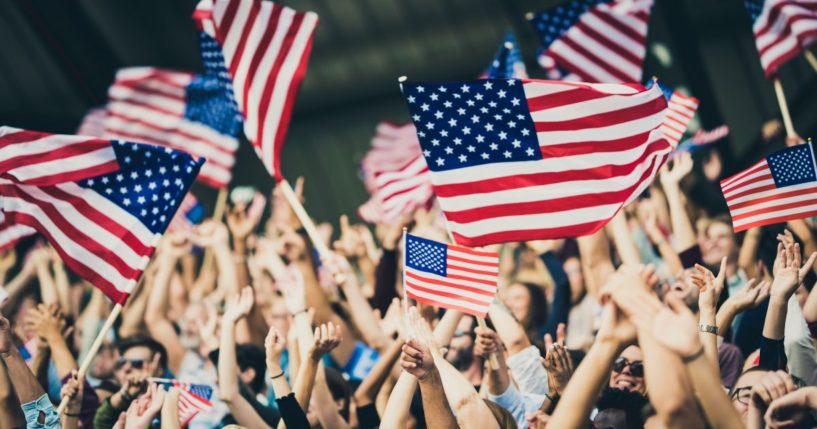 People in a crowd wave American flags in the above stock image.