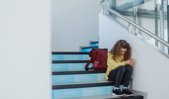 This stock image shows a sad school girl sitting on a staircase.