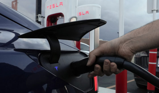 A man plugs in his electric vehicle at a Tesla Supercharger in Detroit, Michigan, on Nov. 16, 2022.