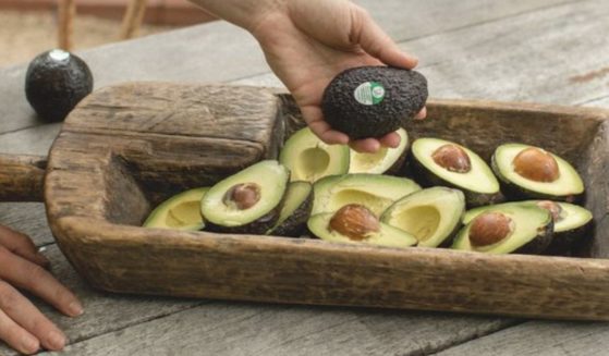 A woman holds an avocado bearing an Apeel label.