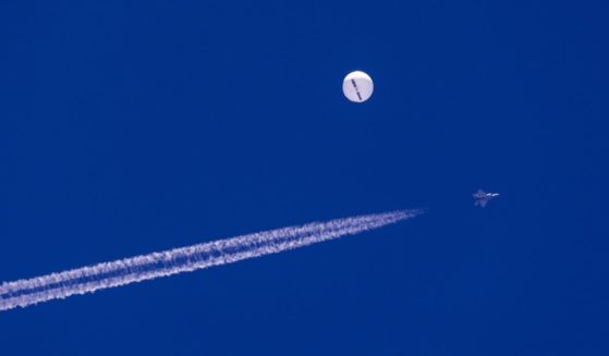 A fighter jet flies near a large balloon drifting above the Atlantic