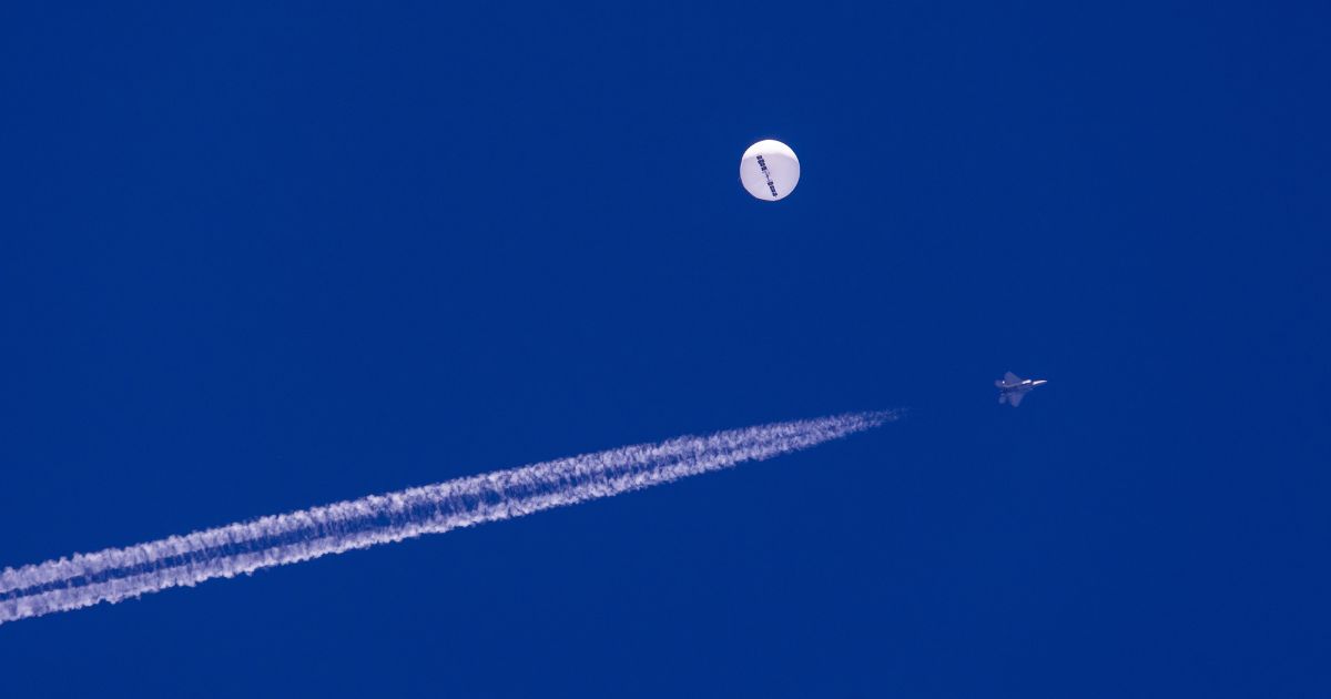 A fighter jet flies near a large balloon drifting above the Atlantic