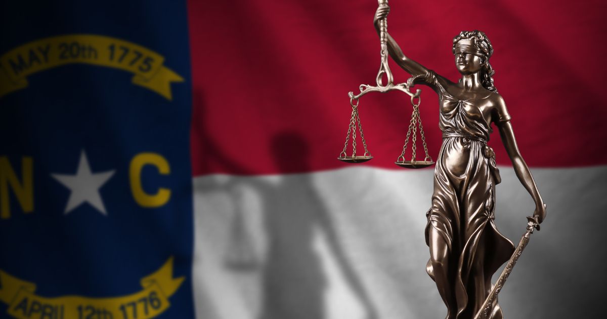 A statue of Lady Justice is seen in front of the North Carolina state flag in the above stock image.