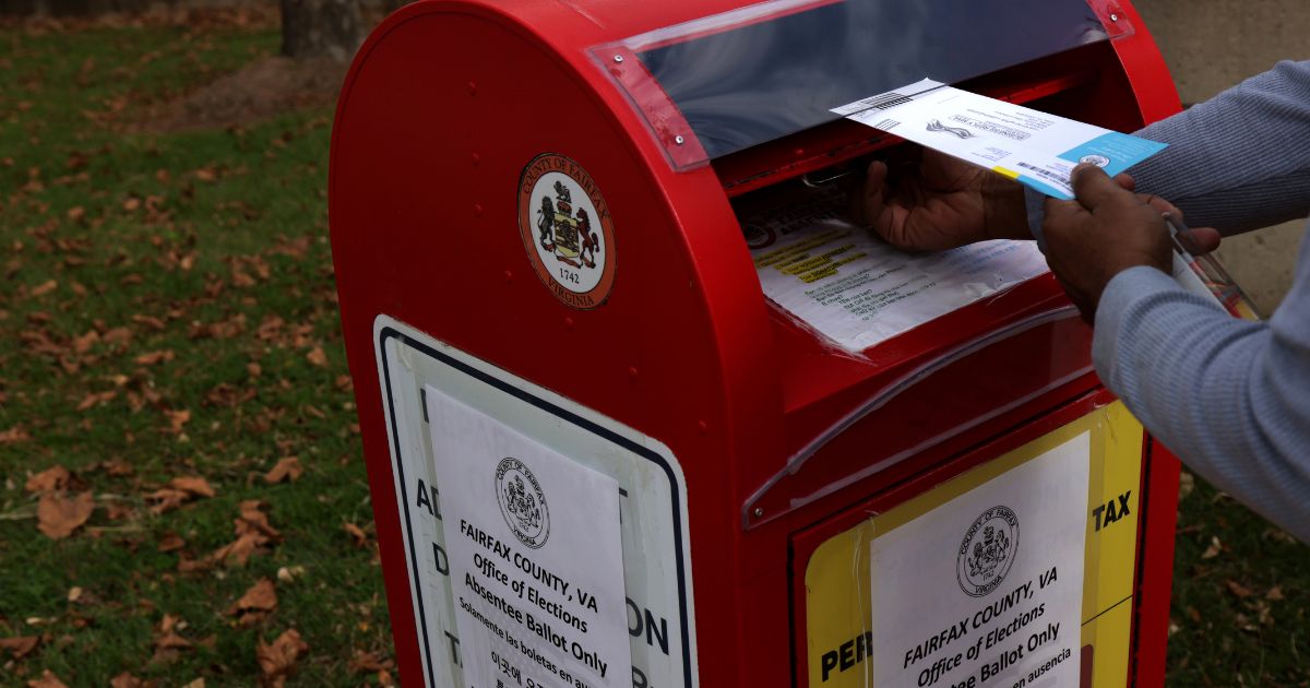 A voter puts an absentee ballot into a collection bin outside the Fairfax County Government Center in Fairfax, Virginia, on Oct. 19, 2020.