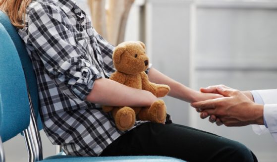 A young girl holds a teddy bear in a doctor's office.