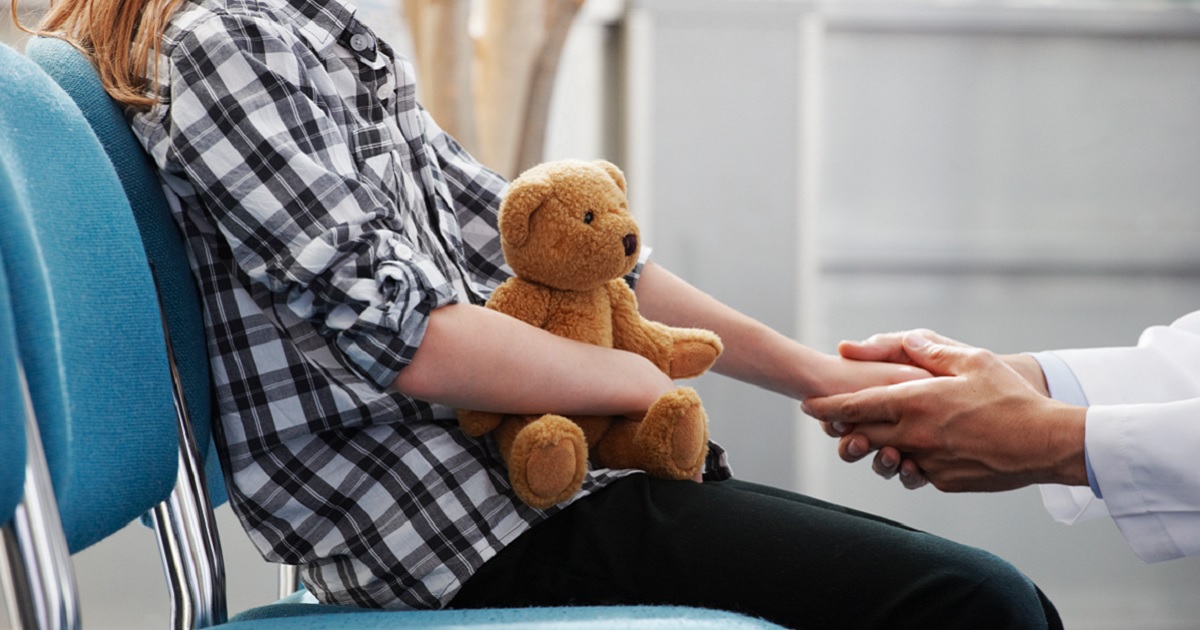 A young girl holds a teddy bear in a doctor's office.