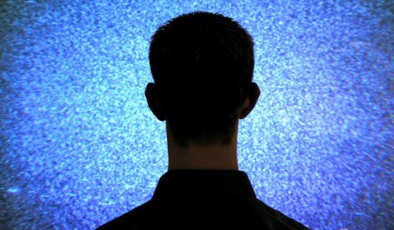 A man sits in front of a television in this stock image.
