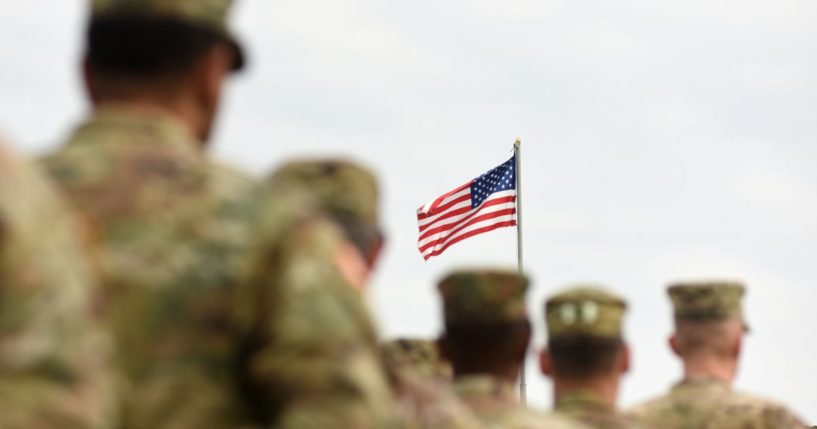 Service members face an American flag in the above stock image.