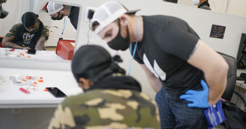 Brian Hackel, right, an overdose prevention specialist, helps Steven Baez, left, a client suffering addiction, find a vein to inject intravenous drugs at an overdose prevention center in New York City on Feb. 18, 2022.