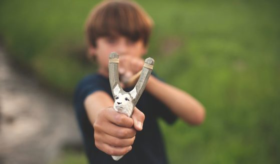 In this stock photo a boy aims a slingshot.