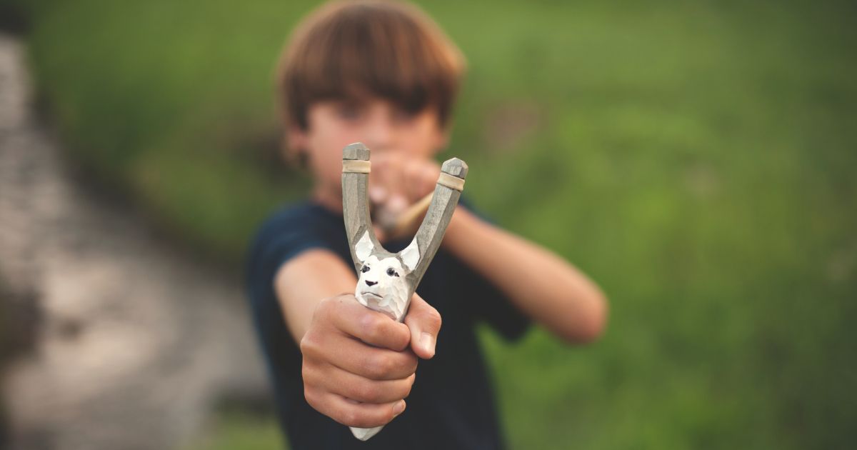 In this stock photo a boy aims a slingshot.