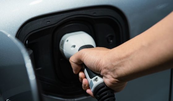 A man charges an electric vehicle in the above stock image.