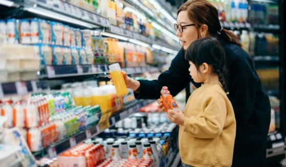 A mother and child select juice from a grocery store aisle in this stock image.