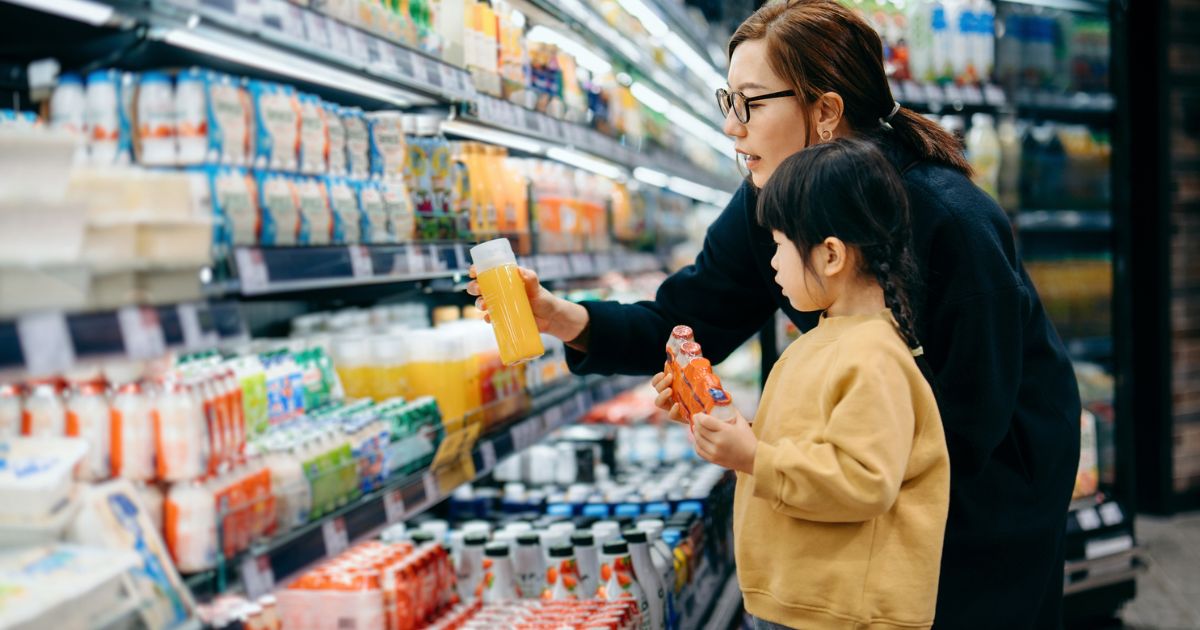 A mother and child select juice from a grocery store aisle in this stock image.