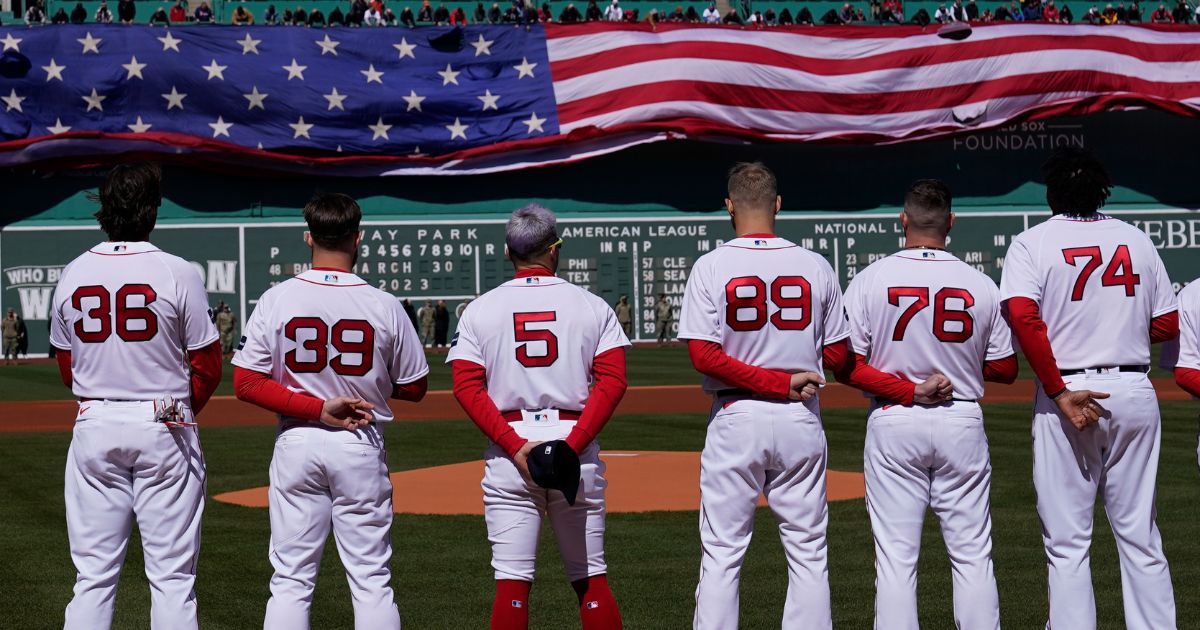 Boston Red Sox players stand for the national anthem as a giant flag is unfurled prior to an opening day baseball game against the Baltimore Orioles, Thursday, March 30, 2023, in Boston. (Charles Krupa / Associated Press)