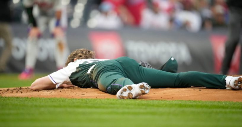 Colorado Rockies starting pitcher Ryan Feltner (18) lays on the mound after getting hit by a single off the bat of Philadelphia Phillies right fielder Nick Castellanos in the second inning of a baseball game Saturday in Denver.