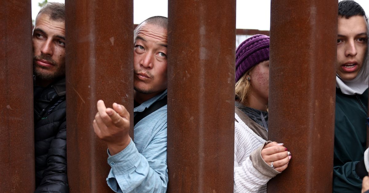 Immigrants seeking asylum in the U.S., who are stuck in a makeshift camp between border walls between the U.S. and Mexico, reach through the border wall on May 12, 2023 in San Diego, California.