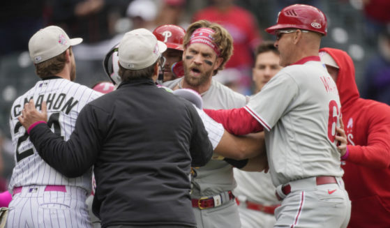 Bryce Harper being restrained by a player, and umpire and a coach