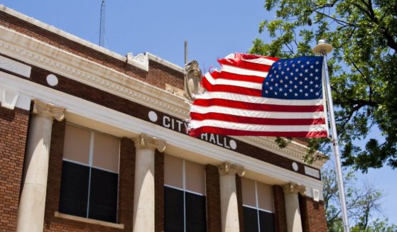 An American flag flies in front of a city hall in this stock image.