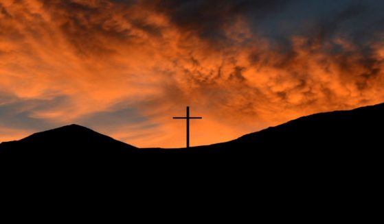 A mountaintop cross is silhouetted against the sunset on the U.S.-Mexican border.