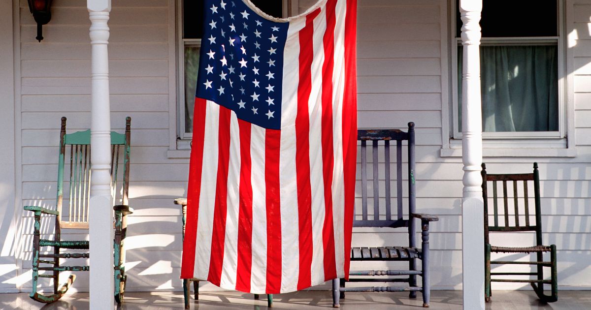 An American flag hangs from a porch in this stock image.