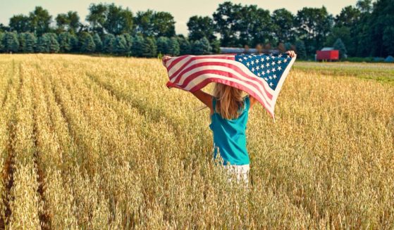 A girl runs in a field with an American flag in this stock image.