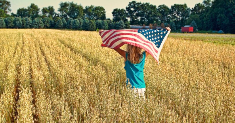 A girl runs in a field with an American flag in this stock image.