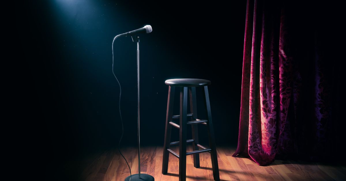 A microphone and stool stand on an empty stage in this stock image.