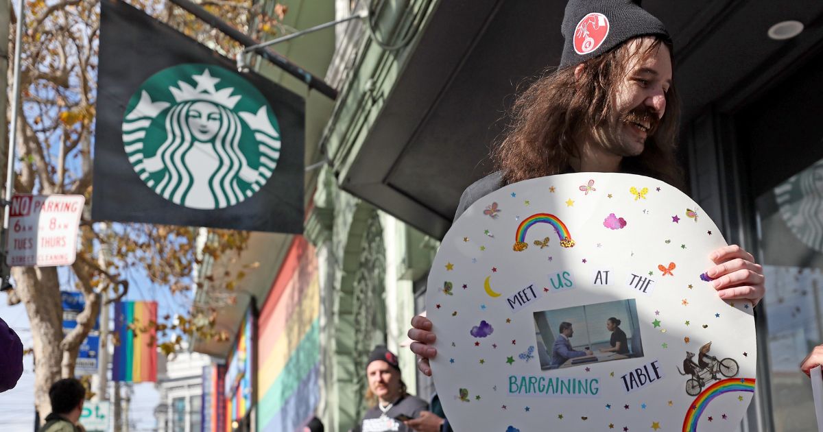 Striking Starbucks worker Kyle Trainer holds a sign outside of a Starbucks coffee shop during a national strike on November 17, 2022 in San Francisco.