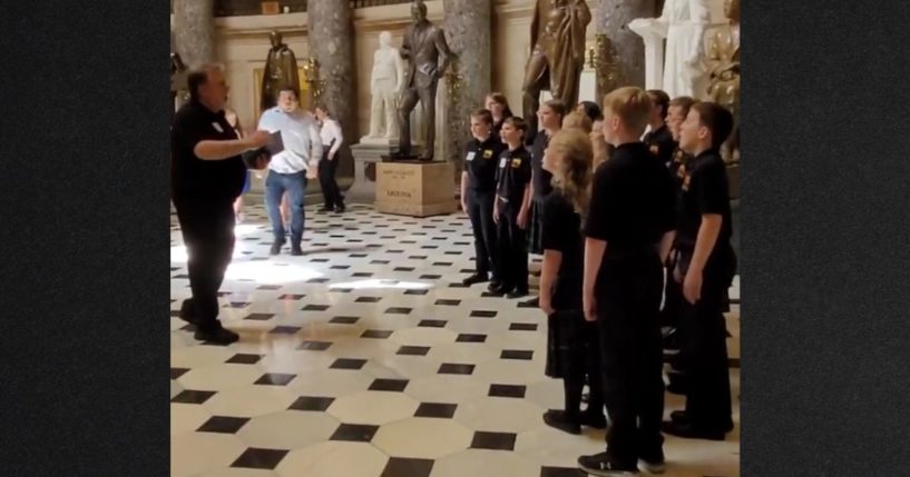 A congressional staffer approaches the choir director to shut down the children's performance at the direction of a Capitol Police officer, seen in the background.