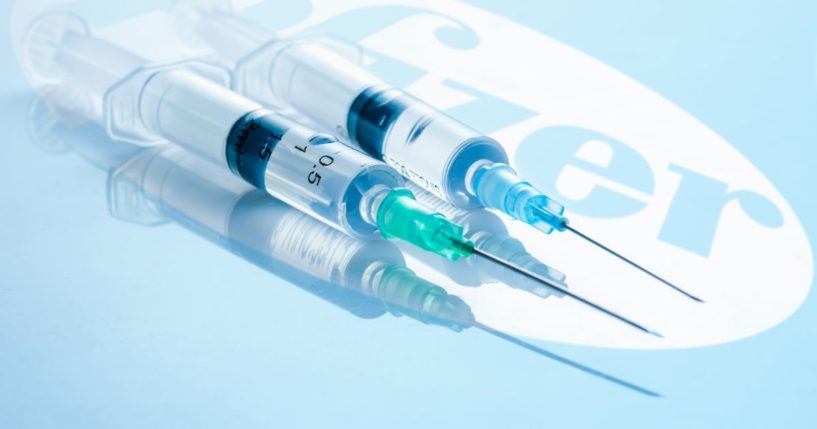 Two syringes of the Pfizer COVID vaccine are pictured above the Pfizer logo.