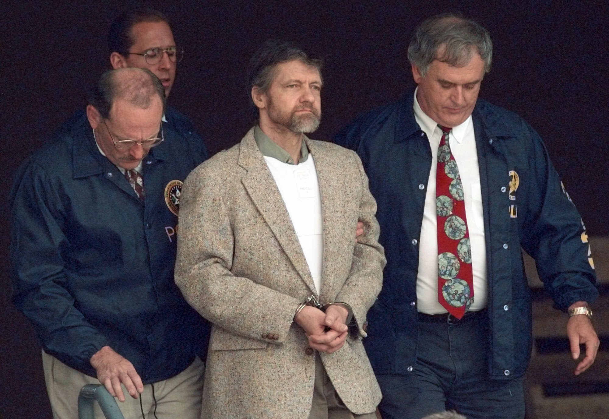 Theodore Kaczynski looks around as U.S. Marshals prepare to take him down the steps at the federal courthouse in Helena, Montana, to a waiting vehicle in a file photo from June 21, 1996. A spokesperson for the Bureau of Prisons told The Associated Press that Kaczynski, known as the “Unabomber,” has died in federal prison.