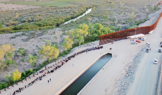 In an aerial view, immigrants seeking asylum in the United States wait in line near the border fence to be processed by U.S. Border Patrol agents after crossing into Arizona from Mexico on May 11 in Yuma, Arizona.