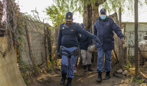 South African police officers remove gas cylinders used by illegal gold miners in the Angelo Informal Settlement in Boksburg, South Africa, Thursday. South African police said at least 17 people, including three children, have died from a leak of a toxic nitrate gas that was being used by illegal miners to process gold.