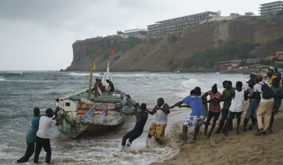 People work together to pull the capsized boat ashore at the beach where several people were found dead in Dakar, Senegal, on Monday.