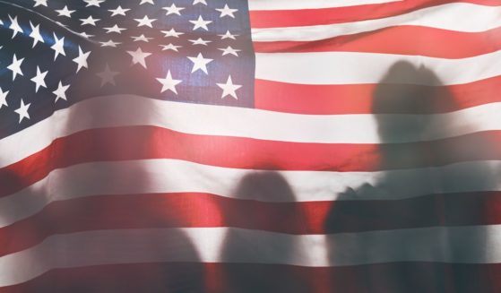 The silhouettes of three people are seen on an American flag in the above stock image.