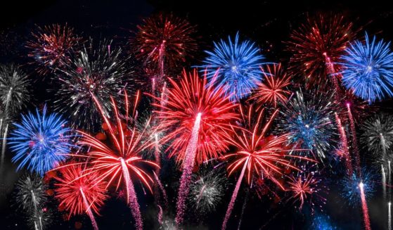Blue, red, and white fireworks light up a dark night sky during an Independence Day celebration.