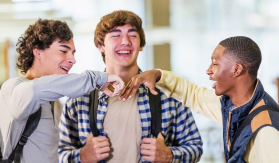 A group of high school-aged boys stand around talking in this stock photo.