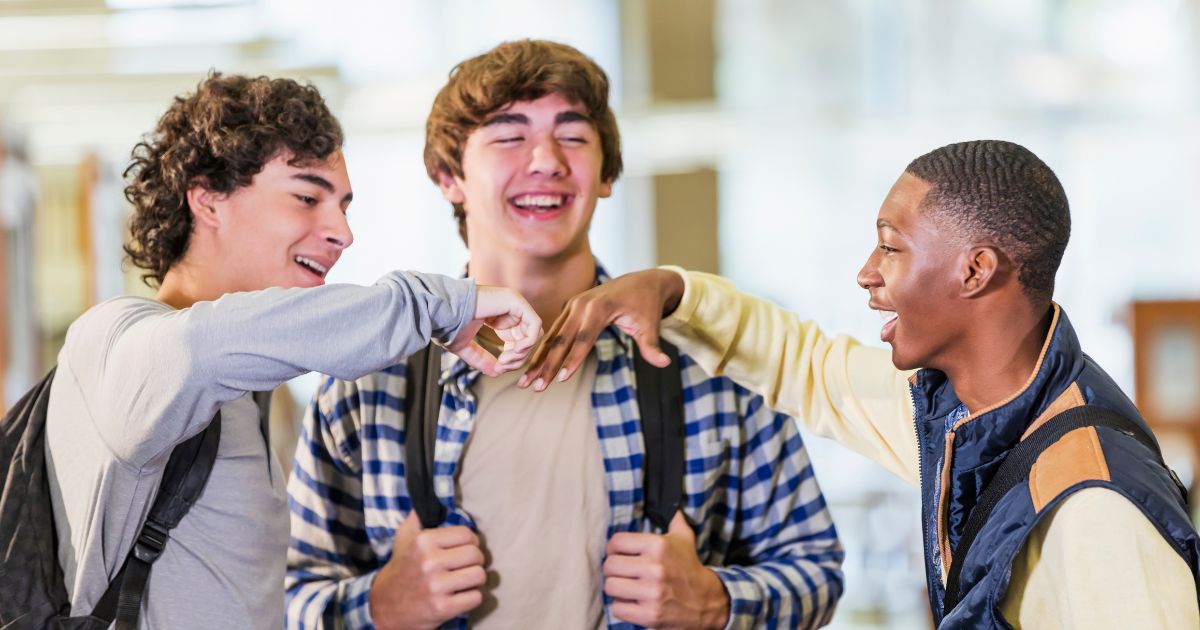 A group of high school-aged boys stand around talking in this stock photo.