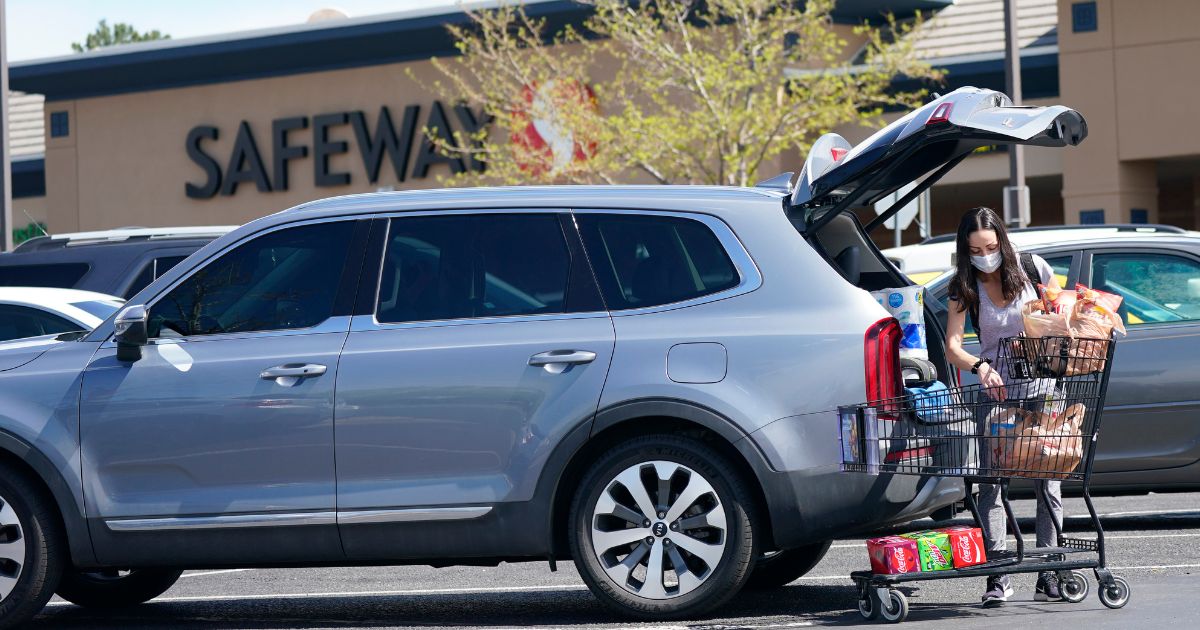 In this photograph, a shopper wearing a face mask loads her purchases into a sports-utility vehicle outside a Safeway grocery store in Aurora, Colo., on May 19, 2021.